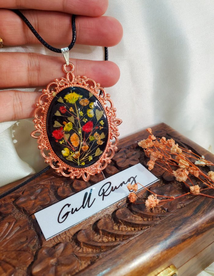 Zar-e-Rung black floral pendant, real flower jewelry, resting on a hand-carved wooden gift box with Gullrung branding